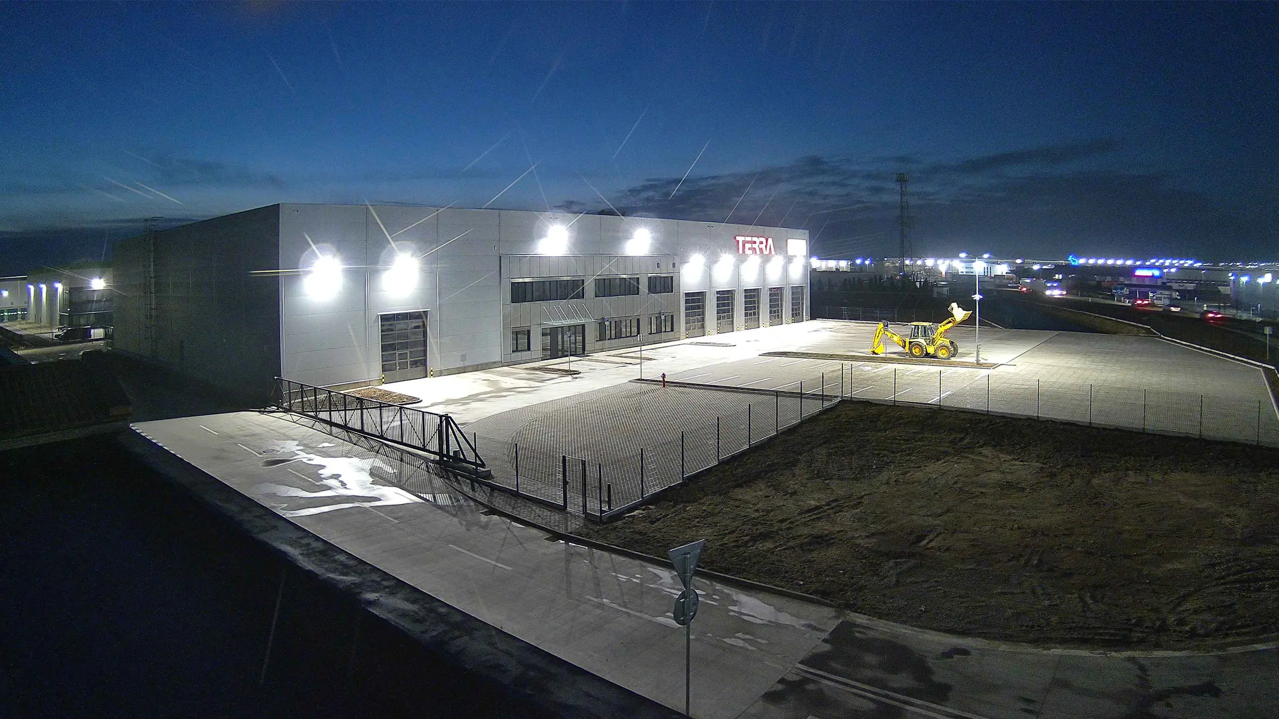Commercial Project D1 Park 2 – a look at the new building of a multi-purpose business and service center with a gray cladding with a large TERRA inscription, a large parking lot and fencing. - obrázok 2