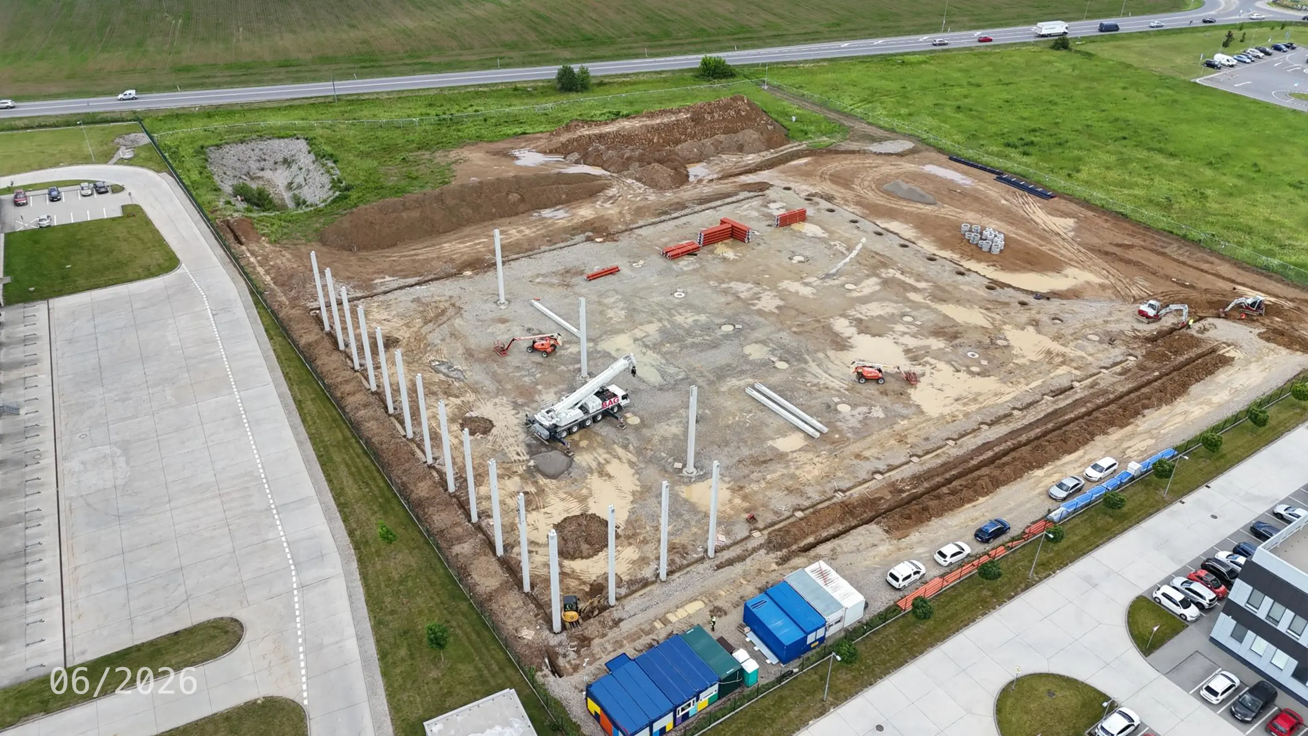 Priemyselný projekt Dubnica 4 – výstavba nosnej konštrukcie novej skladovej a administratívnej haly v Dubnici nad Váhom. Na fotografii sú viditeľné realizované základy a montáž železobetónových stĺpov, ktoré tvoria základ budúceho logistického objektu nadväzujúceho na existujúce budovy priemyselného parku. - obrázok 7