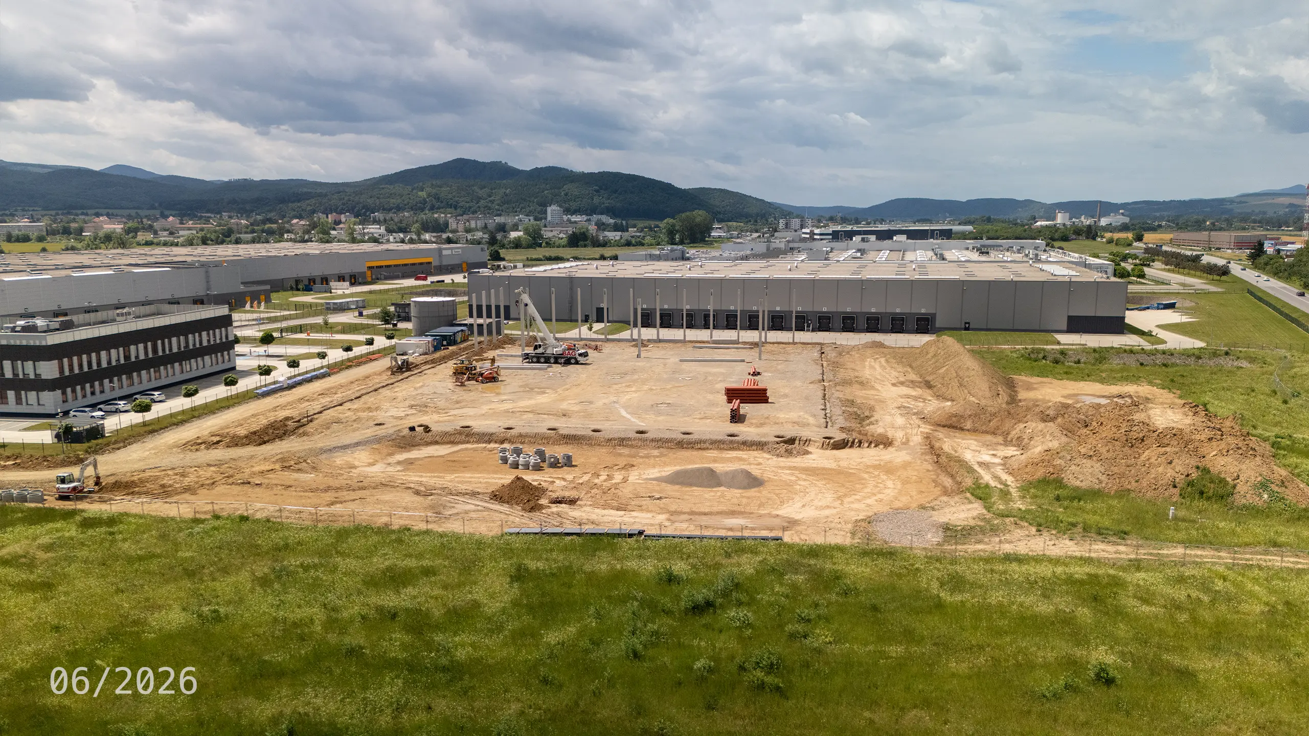Priemyselný projekt Dubnica 4 – výstavba nosnej konštrukcie novej skladovej a administratívnej haly v Dubnici nad Váhom. Na fotografii sú viditeľné realizované základy a montáž železobetónových stĺpov, ktoré tvoria základ budúceho logistického objektu nadväzujúceho na existujúce budovy priemyselného parku. - obrázok 10