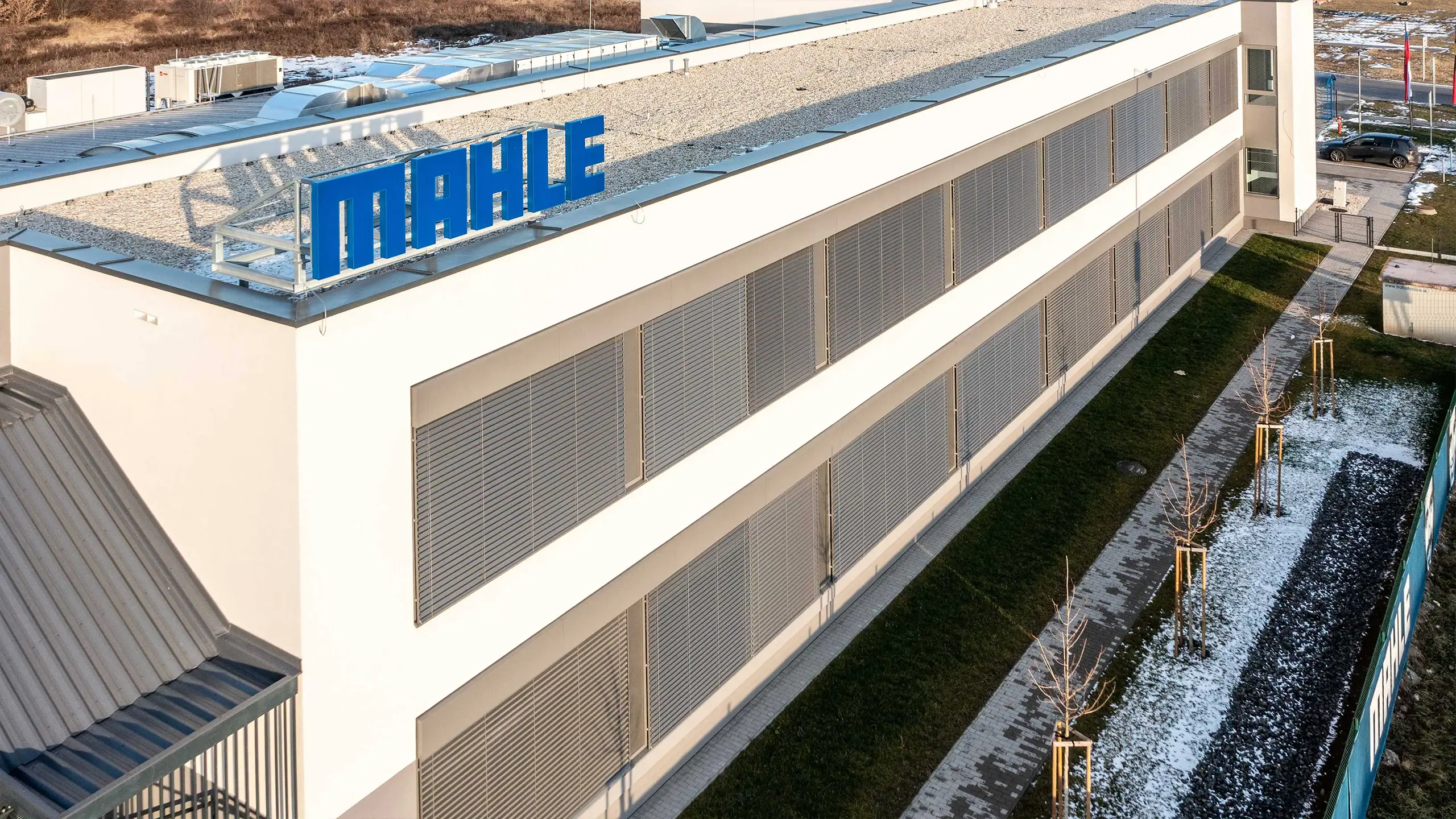 Priemyselný projekt Senica 2 – Bočný pohľad na moderné výskumné a vývojové centrum vybudované pre medzinárodnú automotive spoločnosť. Trojpodlažná budova s modernou fasádou a exteriérovým tienením rozširuje existujúci výrobný a skladový areál určený na vývoj automobilových chladiacich systémov. - obrázok 2