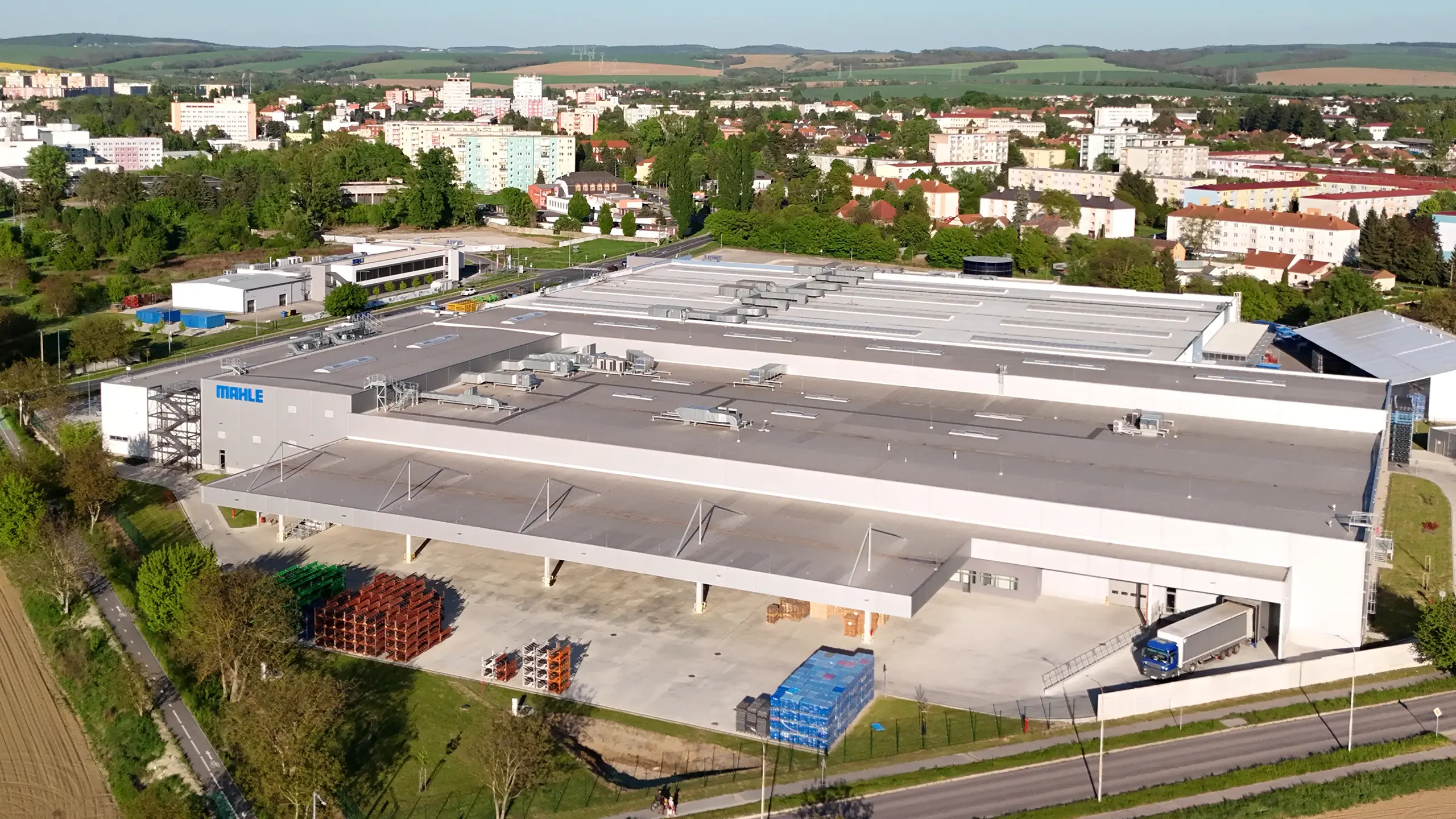 Priemyselný projekt Senica 3 – moderný výrobný a skladovací areál pre medzinárodnú automotive spoločnosť v Senici s rozšírenými výrobnými kapacitami, nakladacími rampami a logistickou infraštruktúrou. Letecký pohľad zachytáva rozsiahlu halu spoločnosti MAHLE v strategickej lokalite s výborným napojením na diaľnicu D2 a dlhodobým rozvojovým potenciálom.