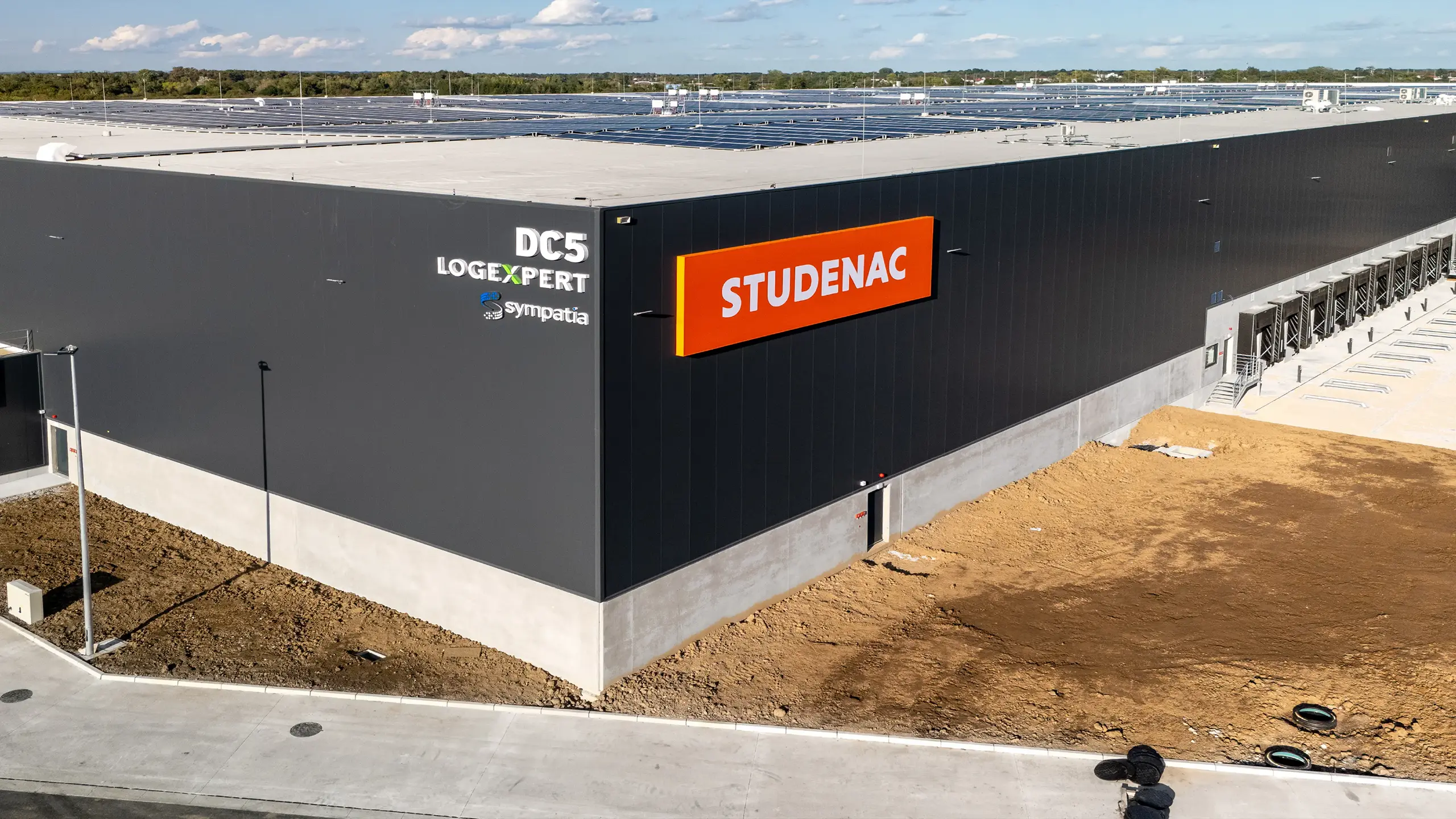 Priemyselný projekt Záhreb 3 – moderná logistická hala novej etapy logistického parku v Záhrebe. Fotografia zachytáva distribučné centrum s nájomcom Studenac, rozsiahlu skladovú halu s nakladacími rampami a fotovoltaickými panelmi na streche, navrhnutú podľa najvyšších štandardov udržateľnosti, energetickej efektívnosti a logistickej prevádzky.