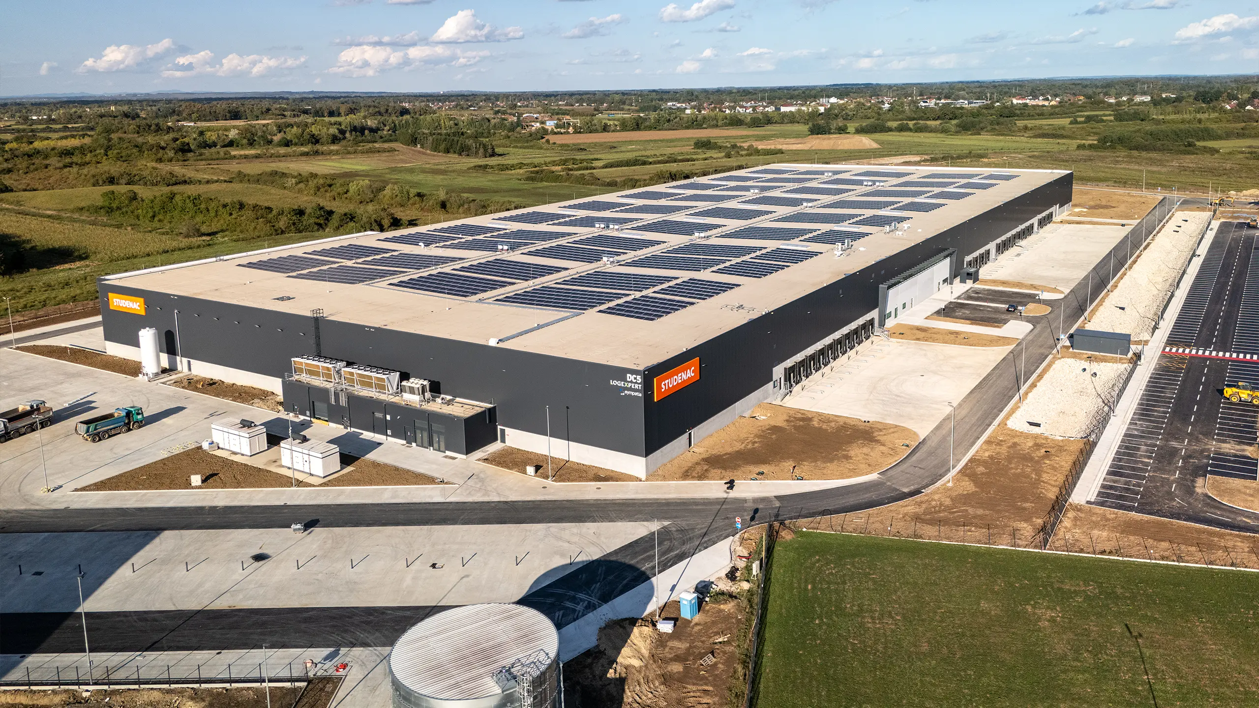 Industrial Project Zagreb 3 – aerial view of a modern logistics facility forming part of the third phase of development in Zagreb. The photograph shows a warehouse building equipped with an extensive rooftop photovoltaic system, logistics infrastructure and handling areas. The project incorporates energy-efficient solutions, BREEAM certification and facilities designed for warehousing, including refrigerated and deep-freeze operations. - obrázok 2