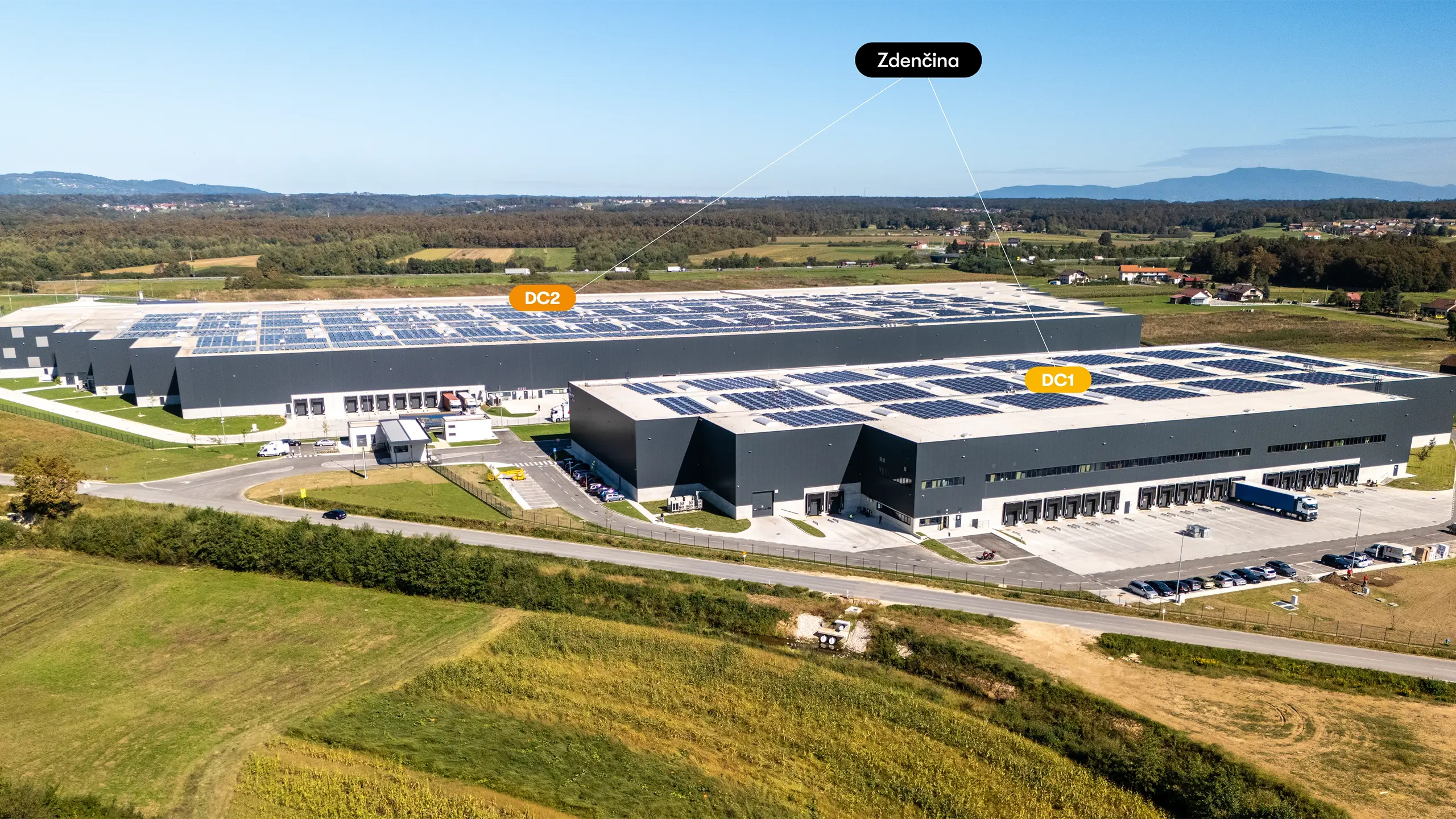Industrial project Zdenčina 1 – aerial view of the regional distribution centre near Zagreb consisting of the DC1 and DC2 buildings. Modern logistics facilities with extensive rooftop photovoltaic systems provide high-standard warehouse and office space. Strategically located next to the A1 motorway, the project meets strict environmental requirements, including BREEAM/LEED certification and the use of renewable energy sources. - obrázok 1