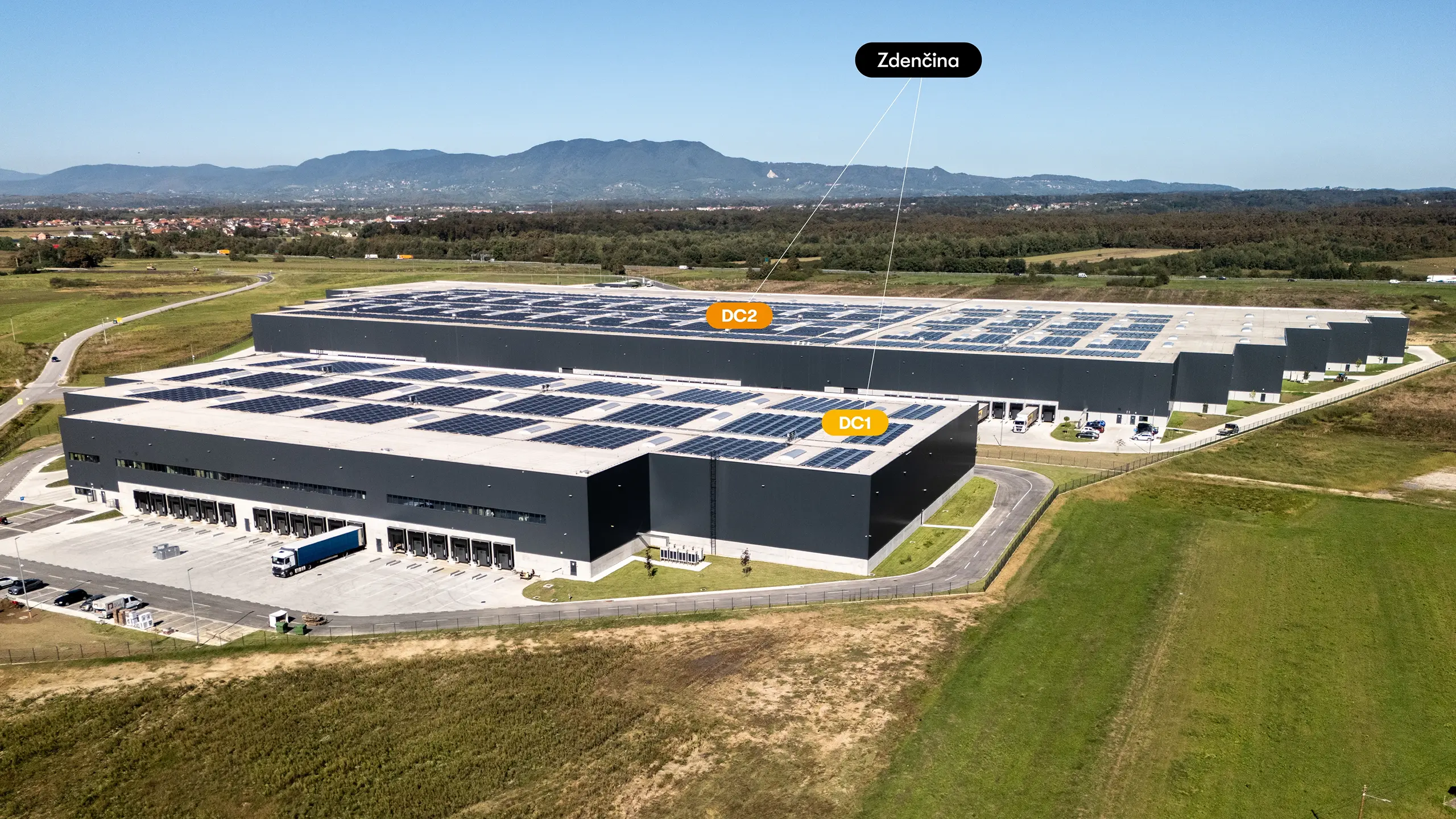 Industrial project Zdenčina 1 – aerial view of the regional distribution centre near Zagreb consisting of the DC1 and DC2 buildings. Modern logistics facilities with extensive rooftop photovoltaic systems provide high-standard warehouse and office space. Strategically located next to the A1 motorway, the project meets strict environmental requirements, including BREEAM/LEED certification and the use of renewable energy sources. - obrázok 3