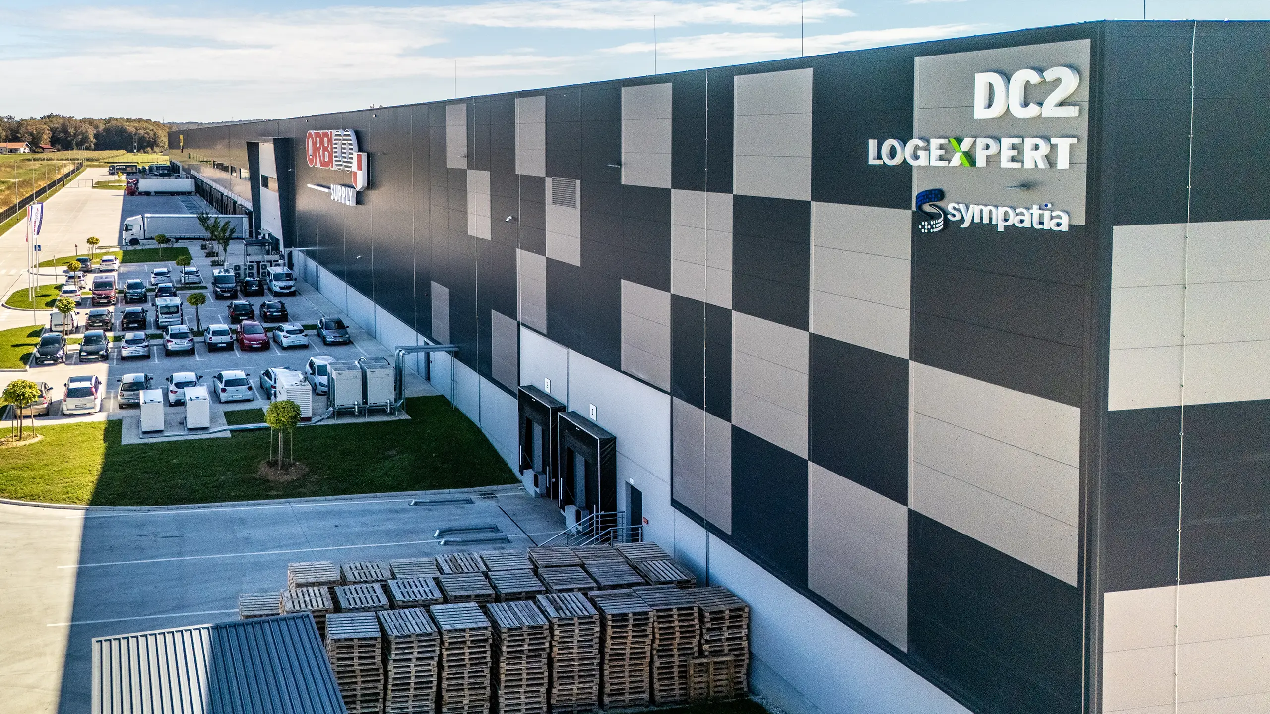 Industrial project Zdenčina 1 – view of the DC2 logistics facility within the regional distribution centre featuring a modern façade and operations of tenant Orbico. The building provides high-quality A-class warehouse space designed according to client requirements, including cross-dock solutions, efficient handling areas and office facilities. The project forms part of a logistics park with excellent access to the A1 motorway and complies with strict environmental standards. - obrázok 8
