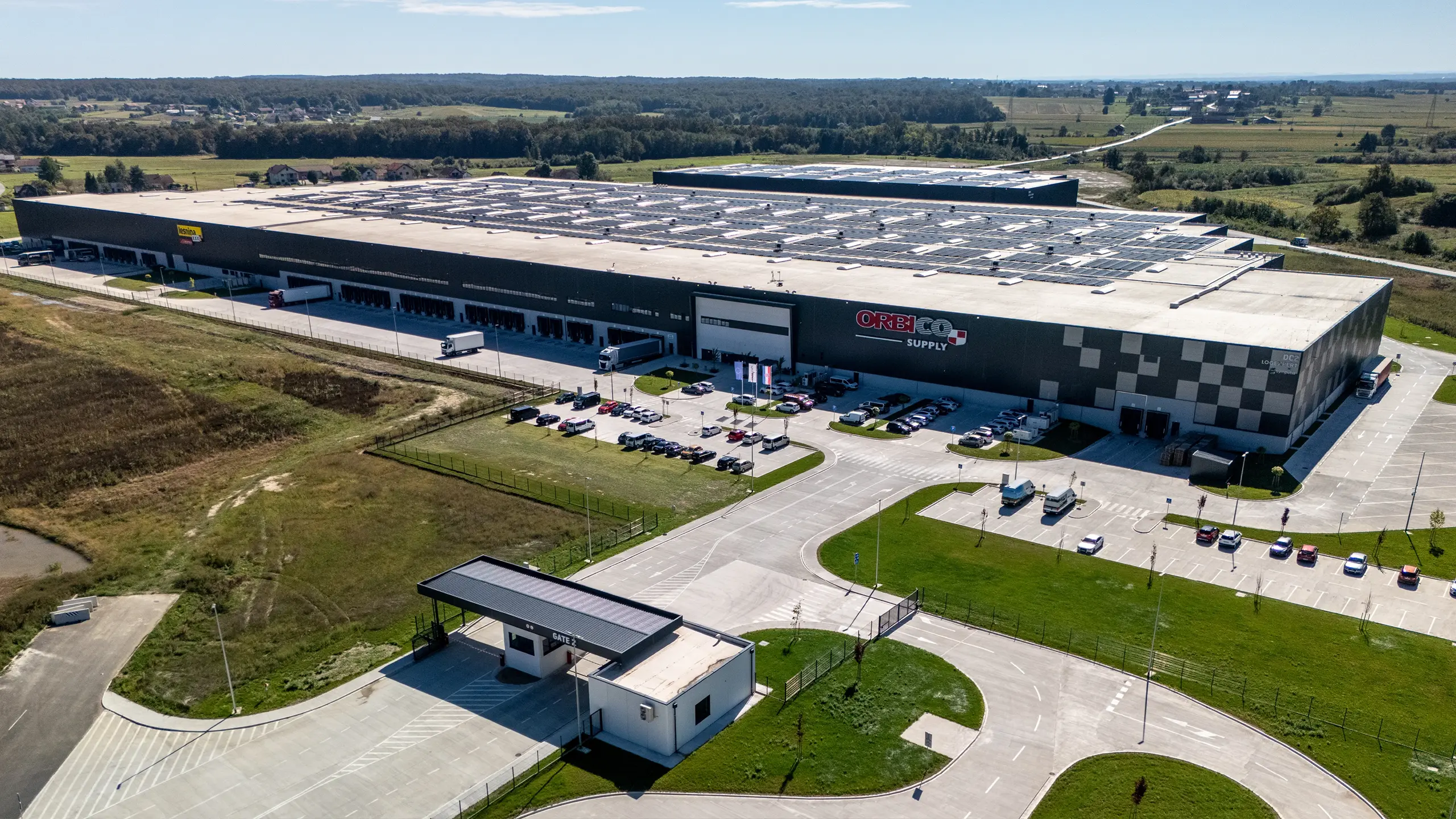Industrial project Zdenčina 1 – view of the DC2 logistics facility within the regional distribution centre featuring a modern façade and operations of tenant Orbico. The building provides high-quality A-class warehouse space designed according to client requirements, including cross-dock solutions, efficient handling areas and office facilities. The project forms part of a logistics park with excellent access to the A1 motorway and complies with strict environmental standards. - obrázok 9