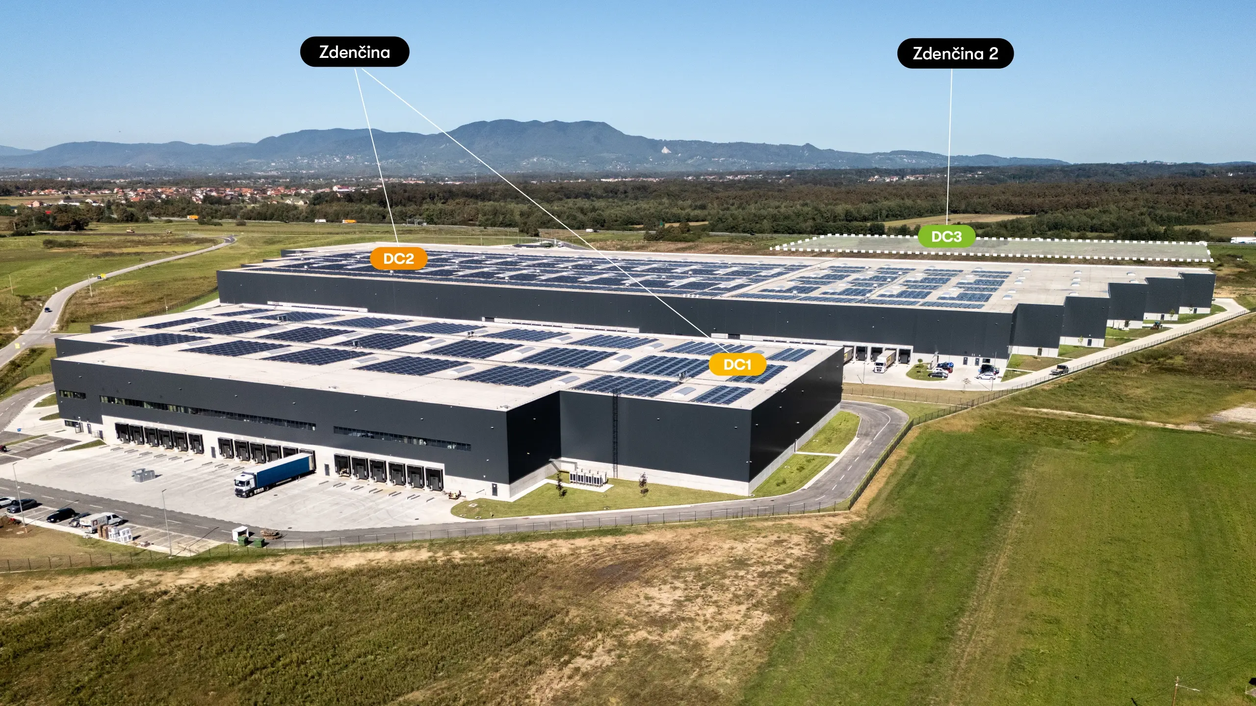 Priemyselný projekt Zdenčina 2 – letecký pohľad na logistický areál Zdenčina s existujúcimi halami DC1 a DC2 a vyznačenou lokalitou budúcej haly DC3 v rámci projektu Zdenčina 2. Projekt nadväzuje na úspešný development Zdenčina 1 a je pripravený na ďalšiu expanziu logistických kapacít pre existujúcich aj budúcich nájomcov. Strategická poloha pri diaľnici A1 a plánované využitie fotovoltaiky, elektromobility a certifikácie BREEAM zabezpečujú vysoký štandard udržateľnej priemyselnej výstavby.